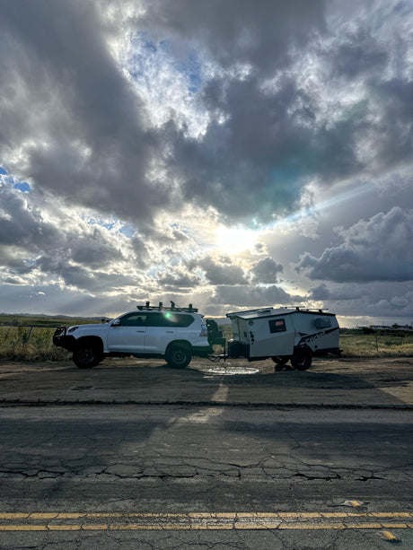Overland SUV towing a Cricket camper, ideal for your next rv rental adventure. Dramatic clouds with sun rays on a dirt road.