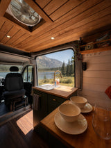 Cozy rv rental interior with a beautiful lake view, featuring a stylish kitchenette and wooden accents, perfect for van life adventures.