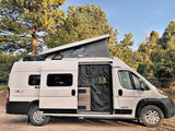 A white camper van with an extended pop-top roof and open side door, parked in a forest. Perfect for an RV rental getaway.