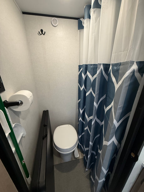 Compact RV rental bathroom with a toilet, shower curtain featuring blue and white geometric patterns, wall hook, and toilet paper.