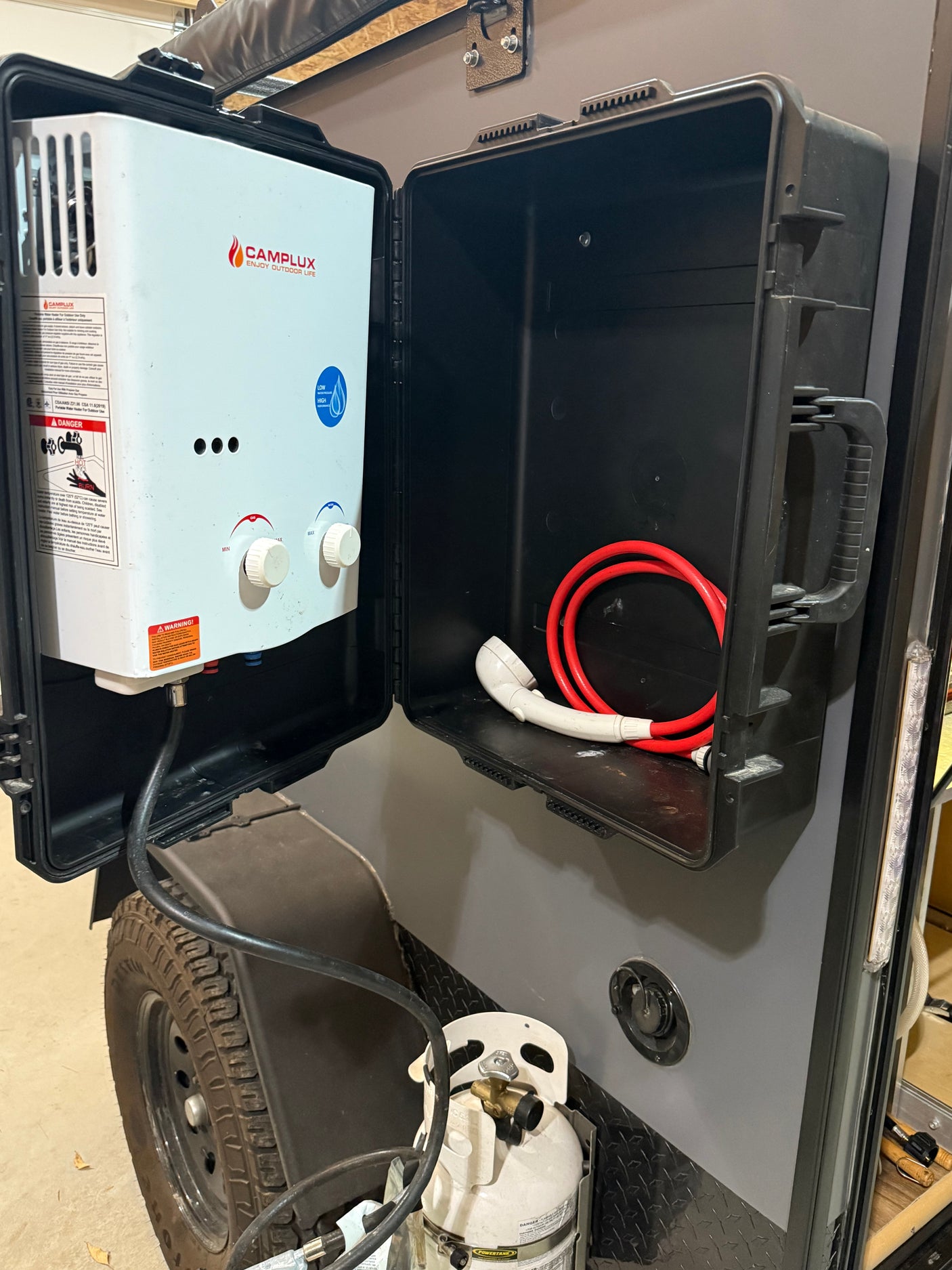 Outdoor shower setup for an RV rental: a Camplux portable water heater, hose, and propane tank on a camper.