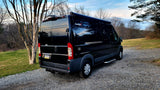 Modern black camper van parked on a gravel drive, perfect for an RV rental getaway. Trees in background.