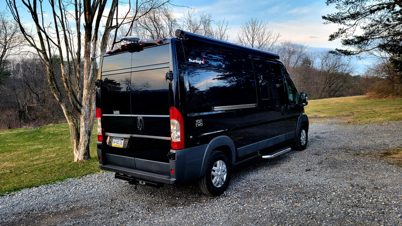 Modern black camper van parked on a gravel drive, perfect for an RV rental getaway. Trees in background. — photo 12