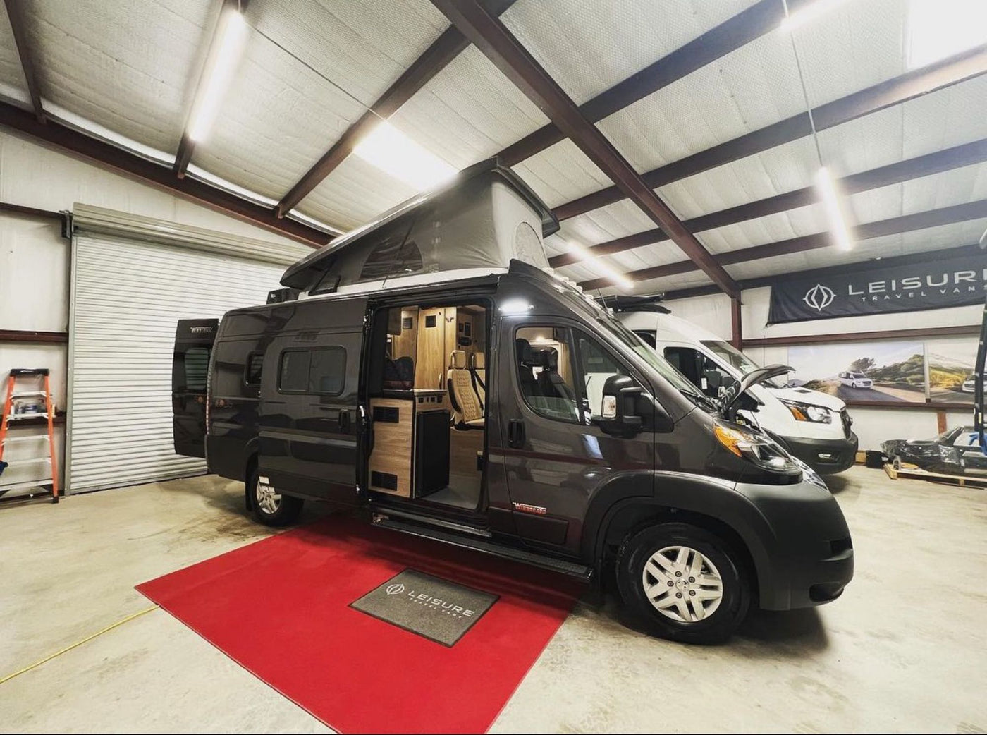  displayed for RV rental. Inside a showroom.|Modern dark gray Winnebago rv rental camper van parked under a residential carport — photo 3