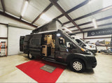 Dark grey pop-top travel van, side door open to reveal interior, displayed for RV rental. Inside a showroom.