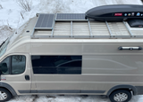 Overhead view of a tan RV rental featuring roof-mounted solar panels and cargo box, parked in snow.