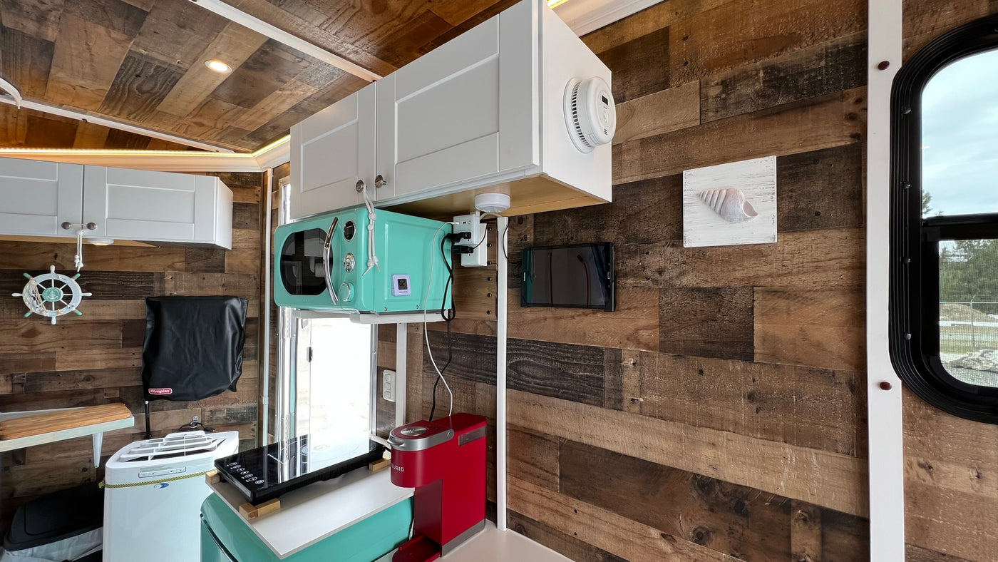 RV rental kitchen: wood walls, white cabinets, retro mint microwave, coffee maker, cooktop, and nautical decor. — photo 9
