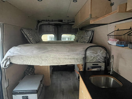 Experience mobile living! This RV rental features a cozy raised bed, compact kitchen with sink, and fridge, ideal for adventures.
