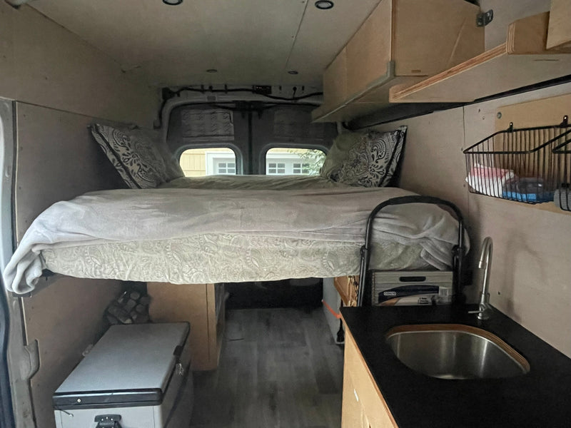 Experience mobile living! This RV rental features a cozy raised bed, compact kitchen with sink, and fridge, ideal for adventures. — photo 5