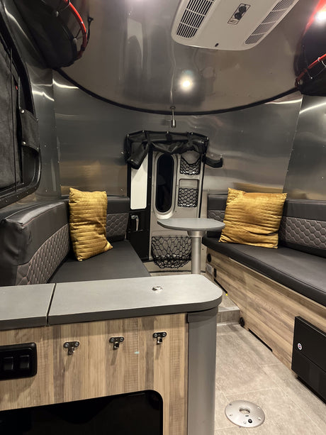 An RV rental's cozy interior, showcasing black and gray upholstered benches, a dinette table, and sleek aluminum walls.
