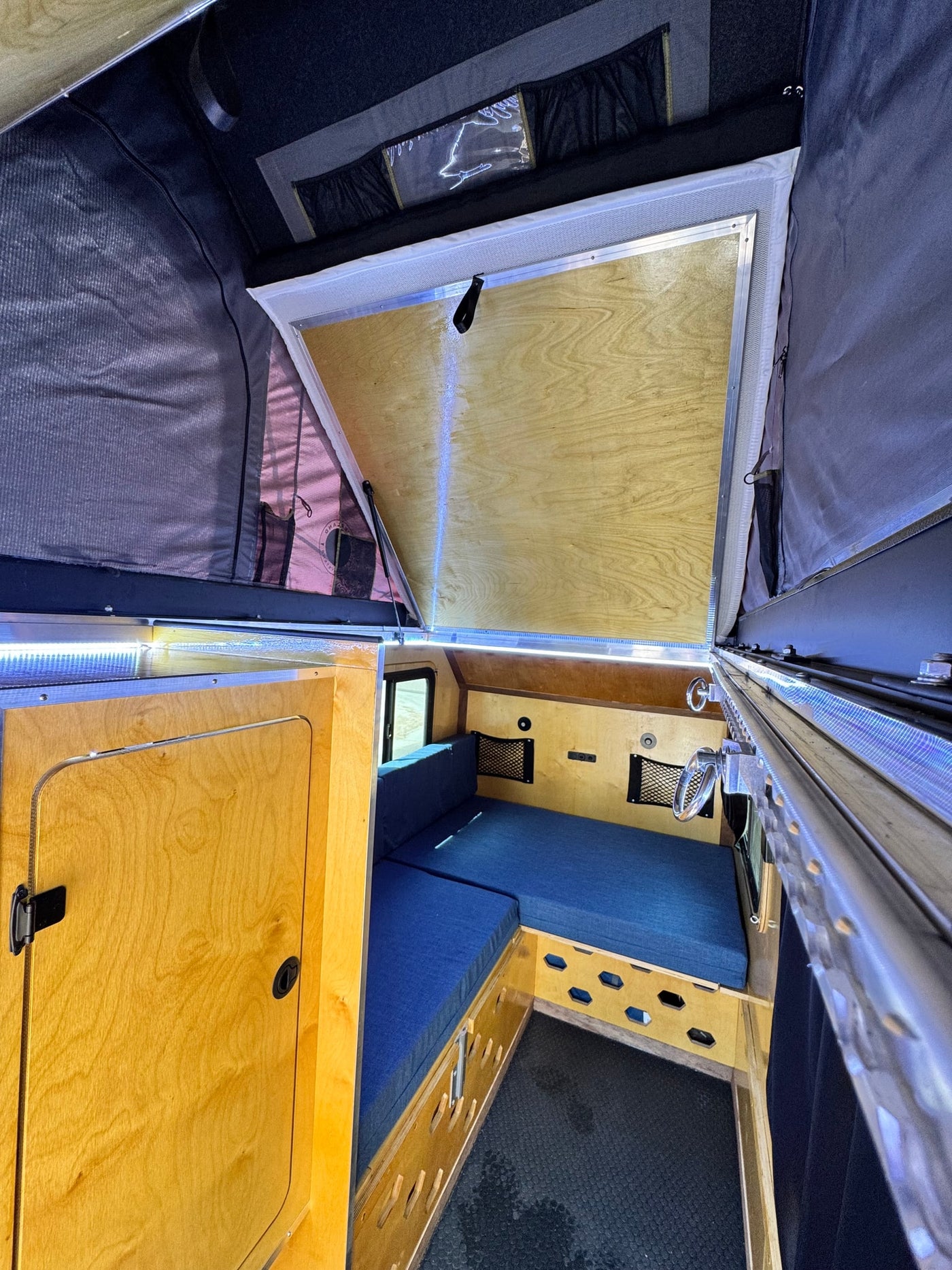 Cozy RV rental interior: blue bed/seating, wooden cabinetry, LED lights, and a pop-up roof with mesh panels. — photo 10