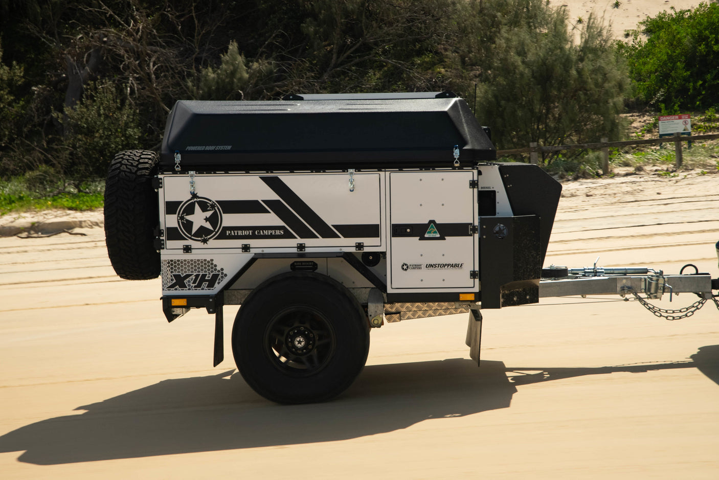 A Patriot Campers XH off-road trailer on a sandy track. This rugged RV rental is ready for your next outdoor adventure.