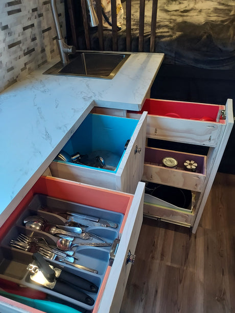 Colorful, compact RV rental kitchen storage with organized pull-out drawers for cutlery and various kitchenware.