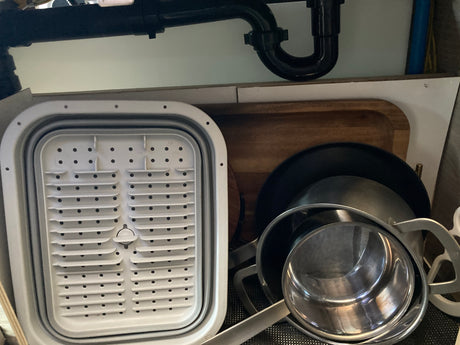 RV rental kitchen: Pots, pans, & a white collapsible dish rack stored under the counter.