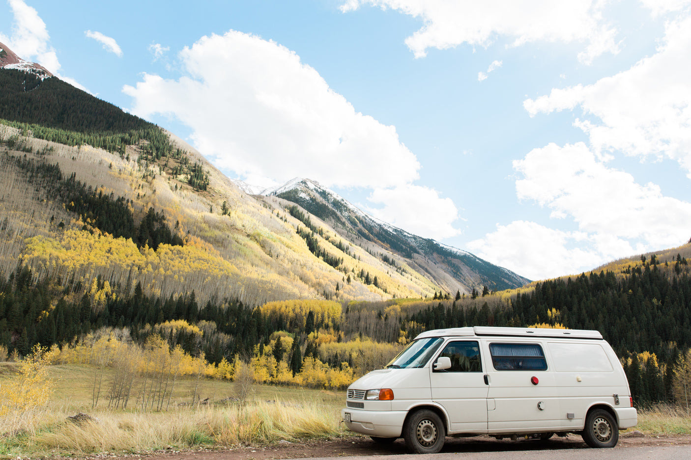 White camper van parked by a mountain road, surrounded by vibrant yellow fall aspens. Perfect for an RV rental adventure.