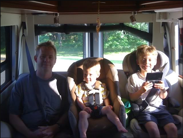 Family enjoying their RV rental: Dad and two boys, one playing a handheld game, are seated inside.