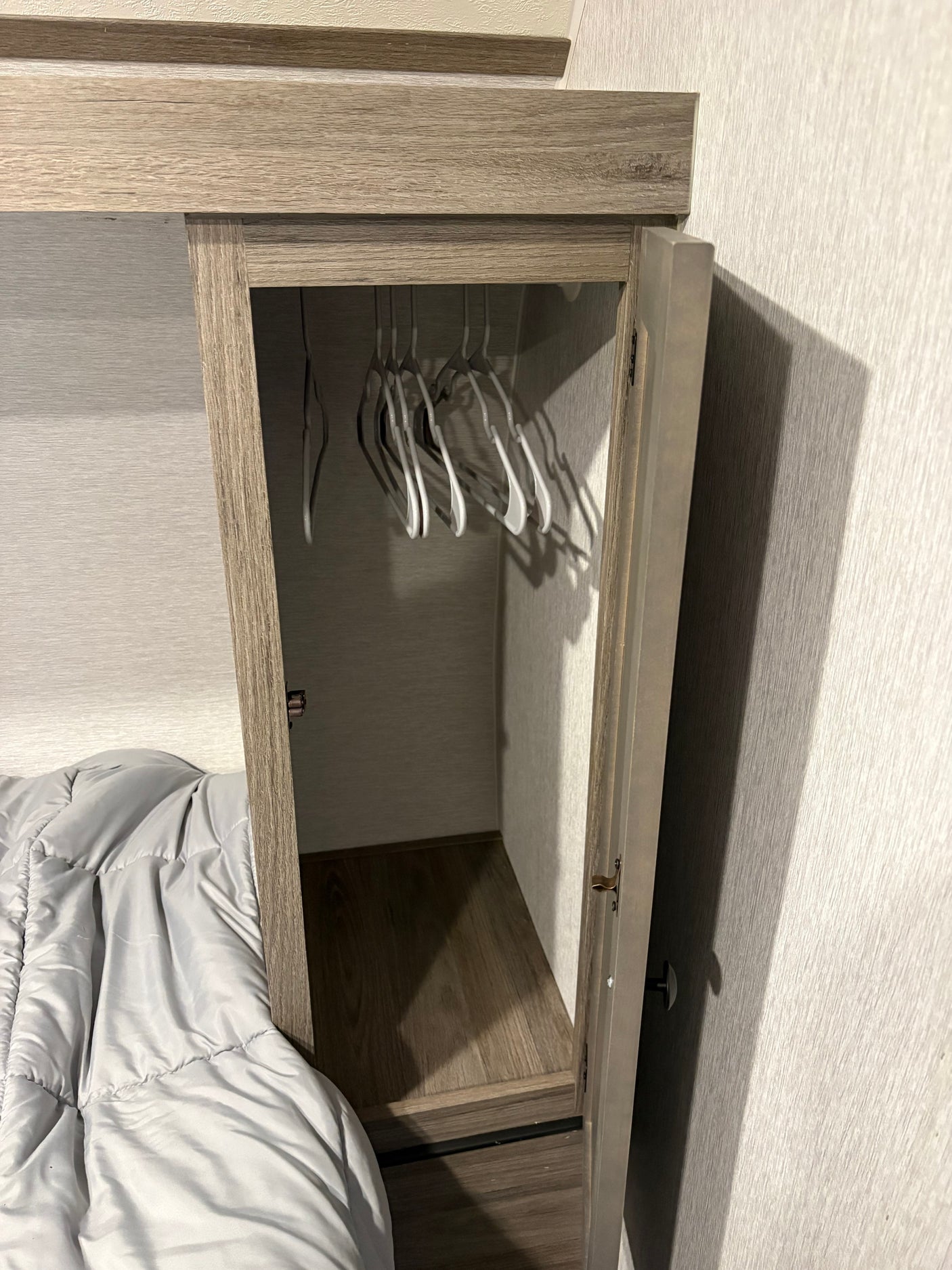 Compact RV rental closet with hangers, adjacent to a bed, offering practical storage in a small space for travelers.
