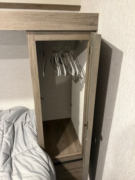 Compact RV rental closet with hangers, adjacent to a bed, offering practical storage in a small space for travelers.