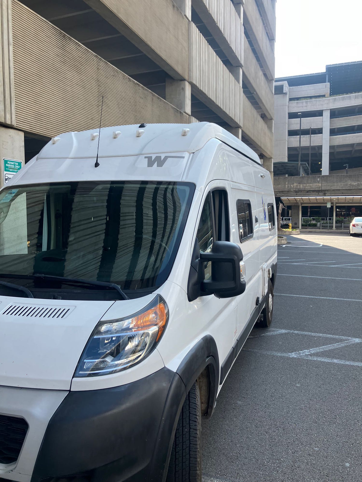 White Winnebago camper van, ideal for your next rv rental, parked in a multi-story concrete garage setting.