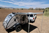 This FREESOLO teardrop camper with its Thule awning extended, hitched to a truck, is an ideal RV rental for mountain adventures.