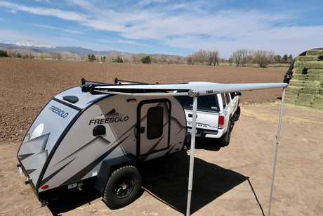 This FREESOLO teardrop camper with its Thule awning extended, hitched to a truck, is an ideal RV rental for mountain adventures.