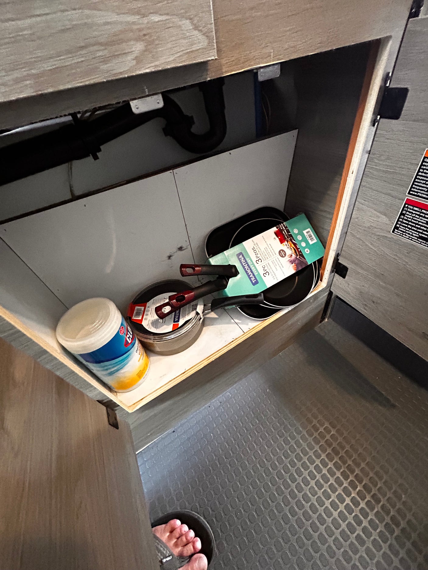 RV rental kitchen cabinet showing new Tramontina pans, Clorox wipes, and a propane warning label for safety.