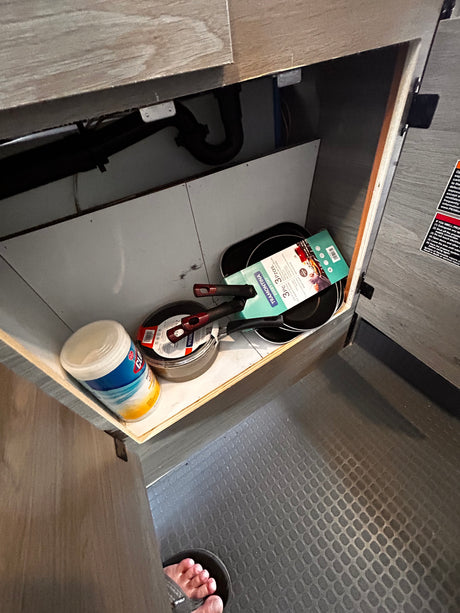 RV rental kitchen cabinet showing new Tramontina pans, Clorox wipes, and a propane warning label for safety.