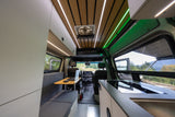 Modern rv rental interior with kitchen, workspace, and scenic outdoor views through windows.