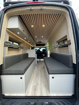 View inside a modern RV rental camper van: light wood ceiling, grey seating benches, and built-in storage. Ideal for travel.
