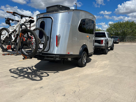 A sleek Airstream travel trailer, equipped with bikes for adventure, is ready for an RV rental trip, towed by a Ford Raptor truck.