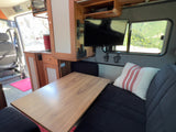 Spacious RV rental interior: cozy seating, table, kitchen, TV, and mountain views from the window. Perfect for van life.