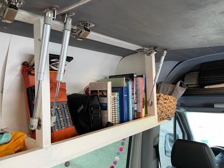 Open overhead storage in an RV rental, neatly filled with books, a Bushnell bag, and travel essentials for the road.
