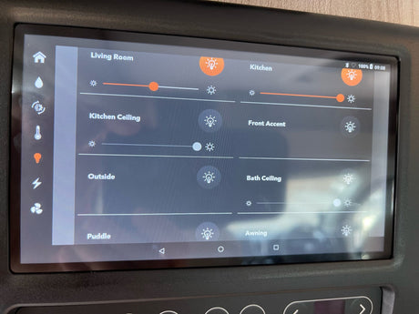 An RV rental's interior smart display shows light controls for living room, kitchen, and exterior, with dimming sliders.