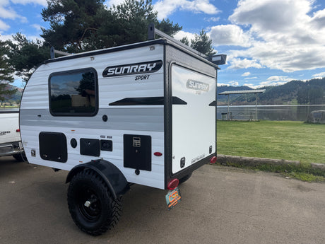 SunRay Sport travel trailer RV rental by a lake, ideal for compact camping adventures with a scenic view.