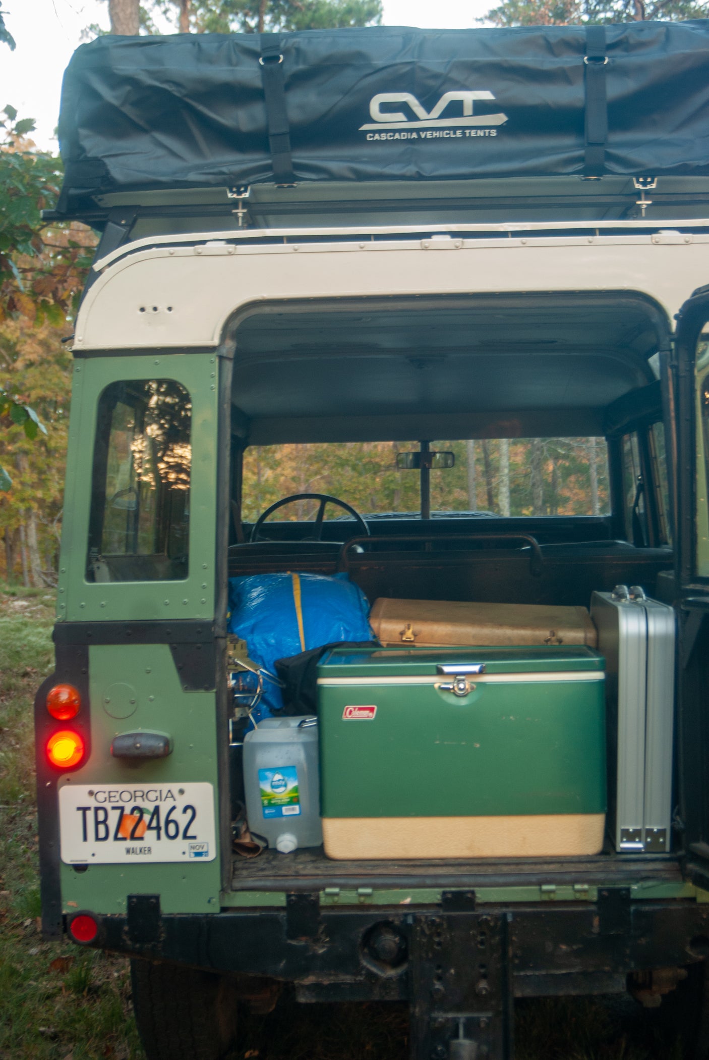Rear of a classic green Land Rover with a black CVT roof tent packed. Camping gear inside, ready for an RV rental adventure!