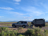 Grey SUV towing an InTech Flyer RV rental on a dirt road, ideal for scenic camping with mountains & sky.