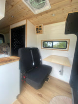 Modern rv rental interior: wood ceiling, white walls, comfortable bench seat, and versatile folding table with controls.
