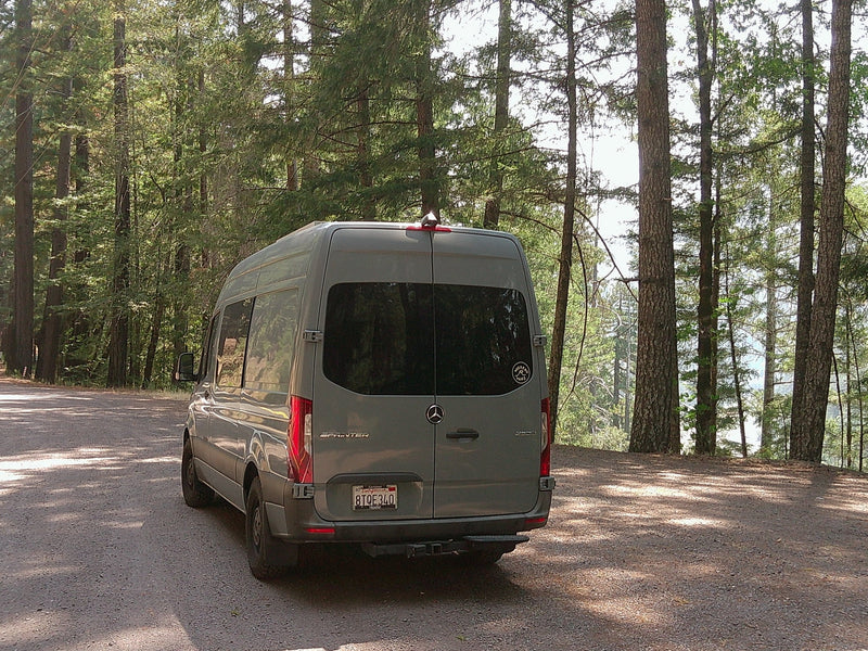 Grey Mercedes Sprinter camper van (RV rental) parked on a forest road with tall trees and a distant lake view.|Spacious RV rental interior featuring seating for 3 — photo 1