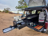 RV rental truck's pull-out kitchen with stove, sink, and outdoor cooking gear. Rooftop tent deployed for camping.