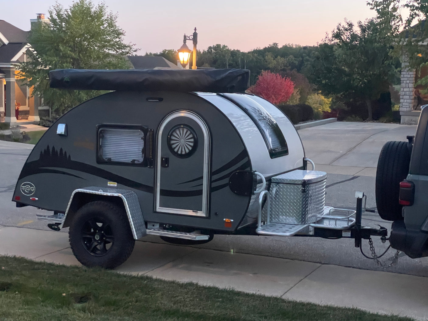 Compact, dark gray teardrop camper, perfect for an RV rental or weekend adventure, parked on a driveway at dusk.