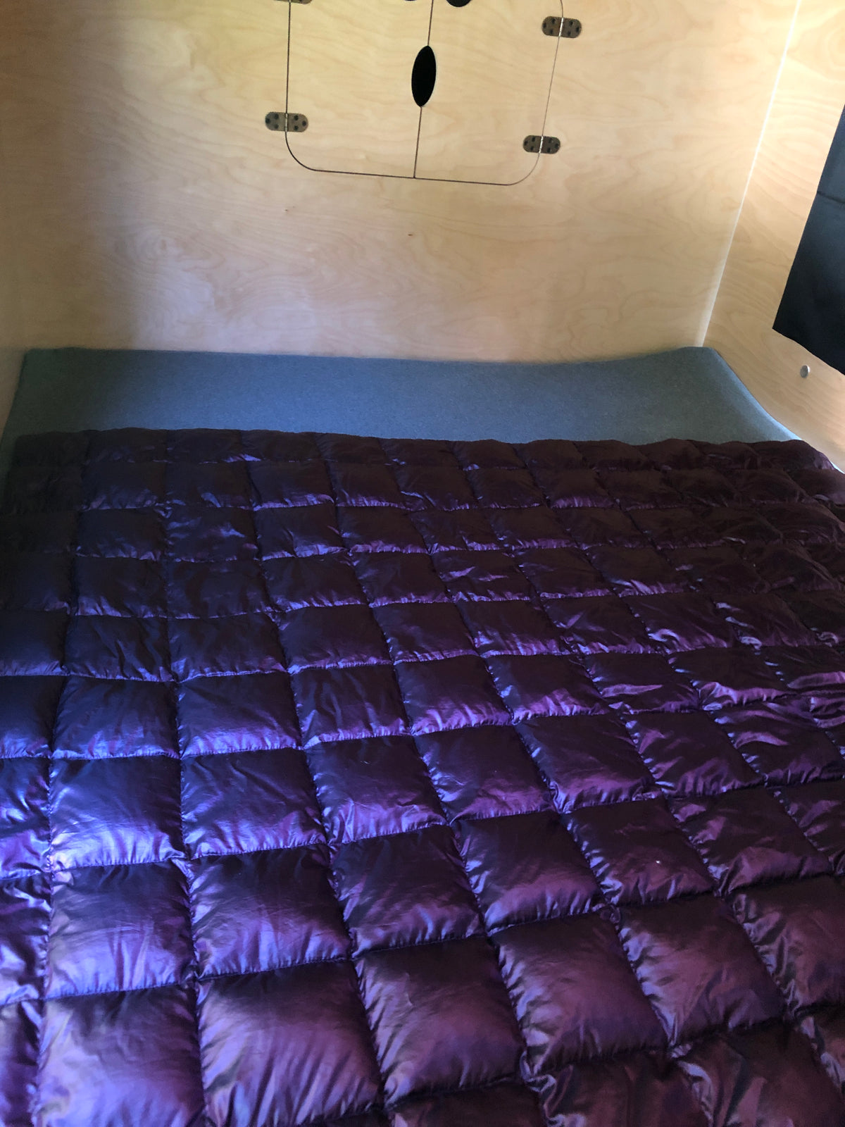 Inside a cozy RV rental: a plush purple quilted blanket on a bed, set against light wood walls with a minimalist design. — photo 6