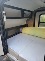 RV rental interior: Comfortable bed with yellow foam topper, overhead storage, and fire extinguisher for safety.