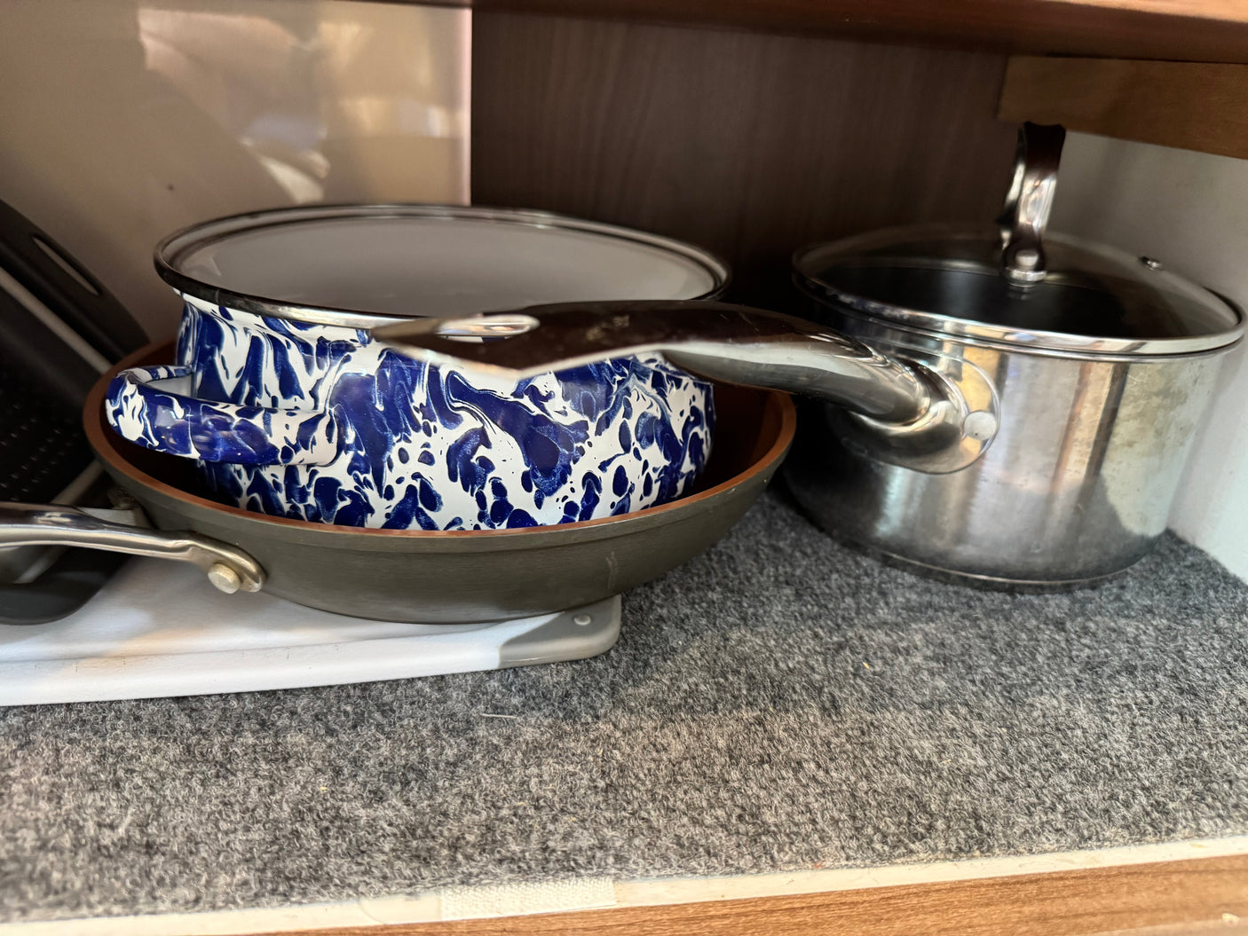 Cooking pots and pans, including a blue enamel pot, frying pan, and stainless steel pot, neatly stored in an RV rental cabinet.