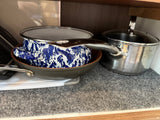 Cooking pots and pans, including a blue enamel pot, frying pan, and stainless steel pot, neatly stored in an RV rental cabinet.