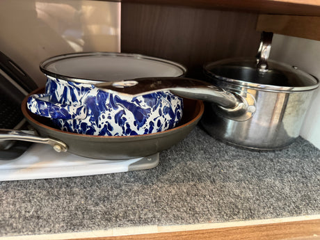 Cooking pots and pans, including a blue enamel pot, frying pan, and stainless steel pot, neatly stored in an RV rental cabinet.