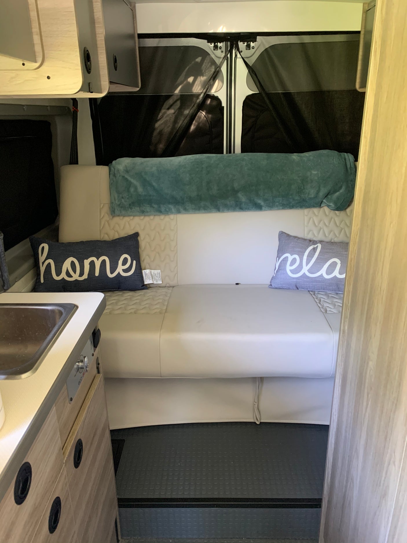 Cozy RV rental interior showcasing a comfortable lounge area with "home" and "relax" pillows, a kitchenette, and storage.