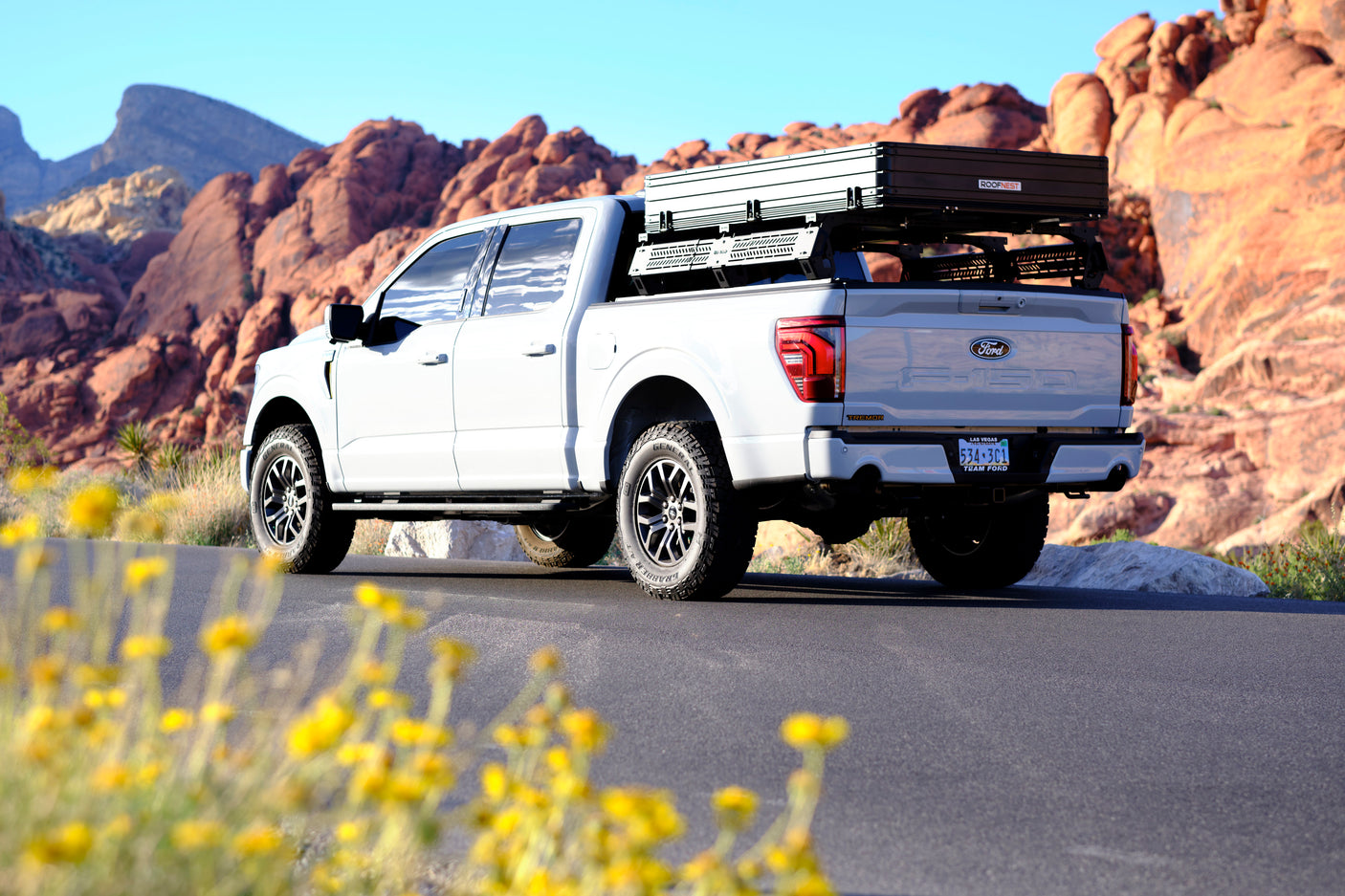 White Ford F-150 Tremor with a rooftop tent & bed rack, parked in red rocks, ready for an **RV rental** style desert camping trip.