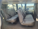 View inside an RV rental shuttle van, showing two rows of grey fabric seats with seatbelts, and RVs visible outside.