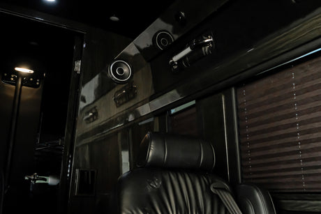 Luxurious RV rental interior with sleek black finishes, comfortable seating, overhead speakers, and privacy blinds.