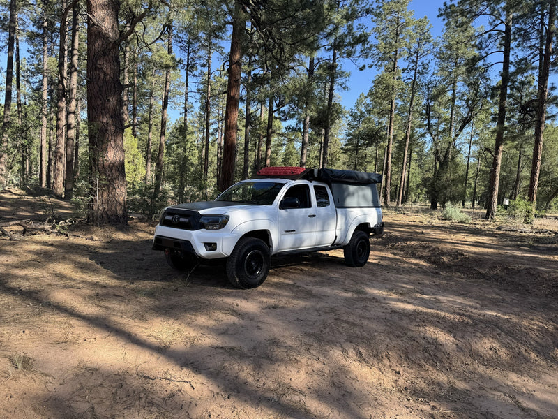 A white Tacoma truck with overlanding camper in a sunny pine forest. Ideal for your next RV rental adventure. — photo 9